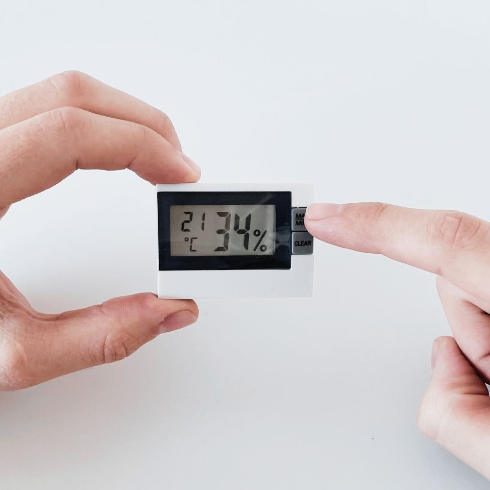 Thermo-/Hygrometer wird in der Handgehalten und ein Finger drückt Knopf